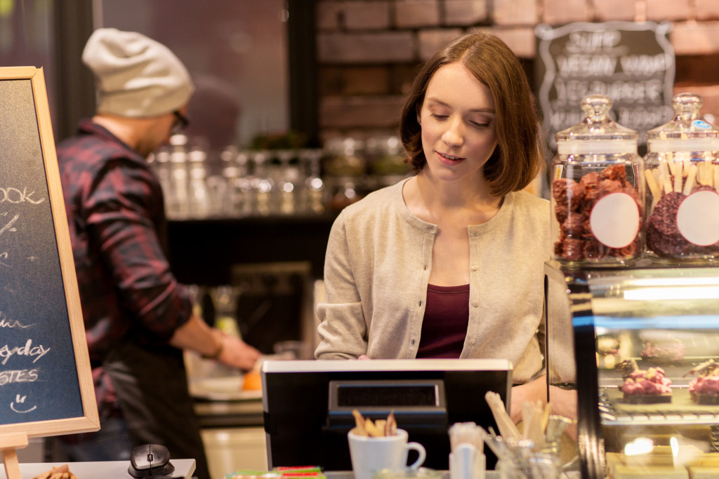 Young female business owner using a register in a cafe.