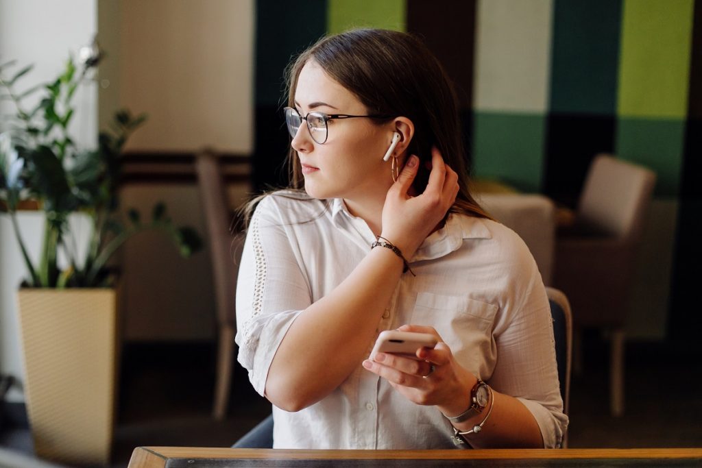 woman with translation earbuds and eyeglasses holding a smartphone