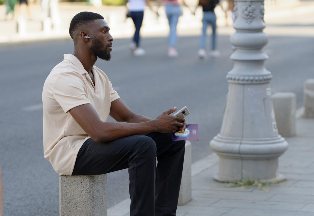 man with earbuds and a phone sitting thoughtfully at the side of the road