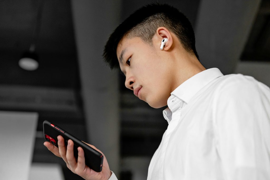 Asian man wearing earbuds and looking down, scrolling on his phone